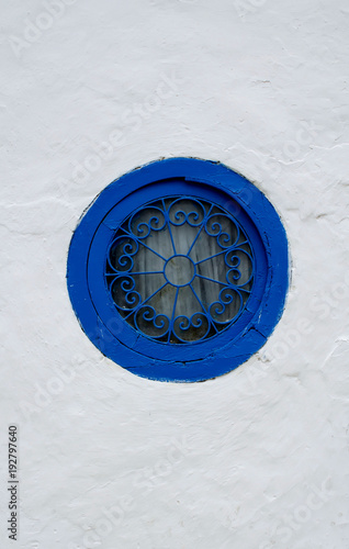 Round window with a blue frame with a patterned grille on a white wall photo