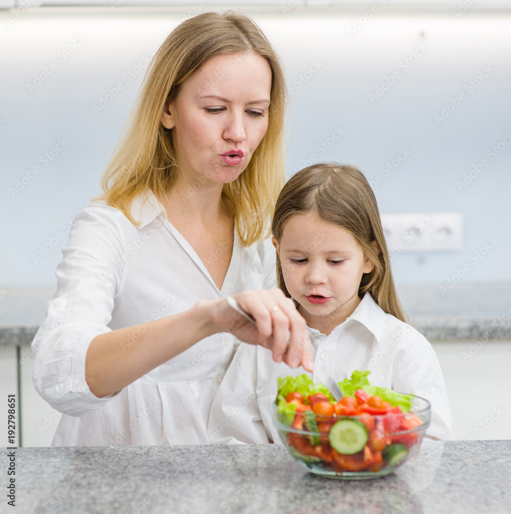 mother and daughter eating salad in the kitchen