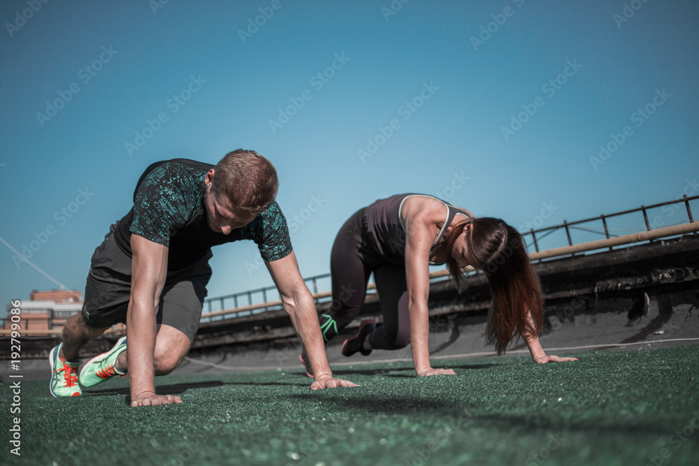 Man and woman working out together on abs muscles. Couple trianing on the roof of the building.