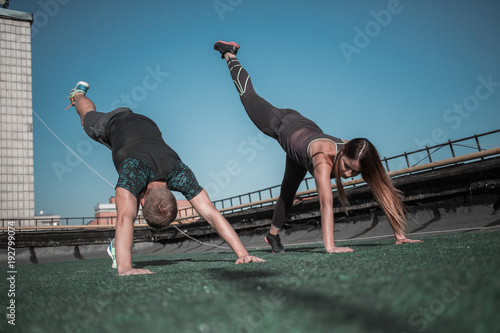 Sportive people doing sport exercises on the roof of the building. Young man and woman working out together. photo