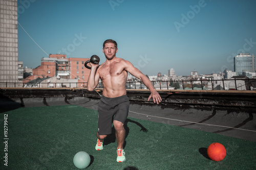 Man practicing crossfit exercises with weight. Sport on the roof, athletic guy lifting weight with one hand. © Svyatoslav Lypynskyy