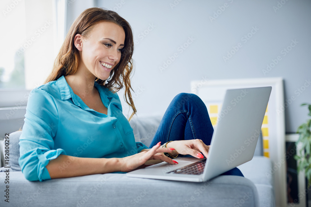 Side view of a beautiful young woman using laptop and sitting on sofa at home Side view of a beautiful young woman using laptop and sitting on sofa at home