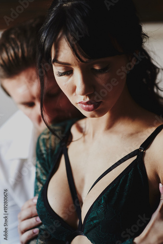 Strong Man and beautiful woman lying on the bed intimate atmosphere. Luxurious furniture and beautiful interior. A girl with black hair is a man without a shirt. Love and tenderness.