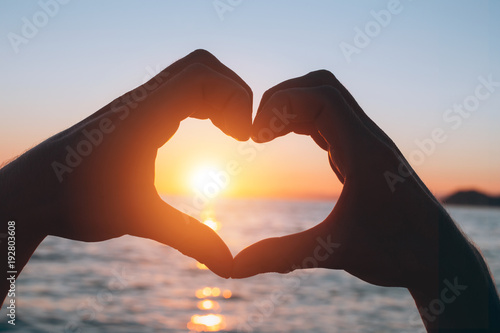 Male hands in a heart shape at sunset