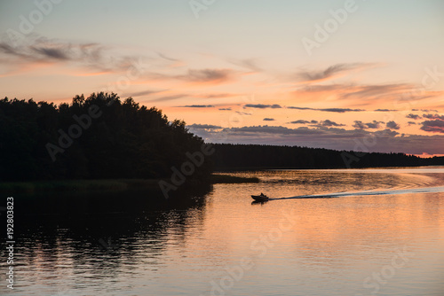 Modern russian village in national russian style on the lake coast. Good place for camping, fishing, hunting and relax. Summer sunset sky reflection in calm warm water.