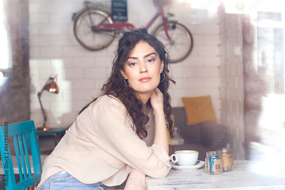 Young woman sitting by the cafe table and drinking coffee Young woman sitting by the cafe table and drinking coffee