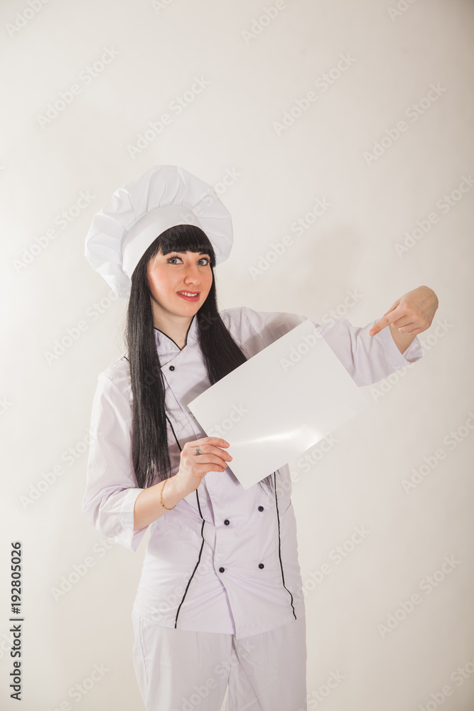 Young girl in the clothes of the cook. Confectioner on a white background. The cook holds a white inscription label Young girl in the clothes of the cook. Confectioner on a white background. The cook holds a white inscription label