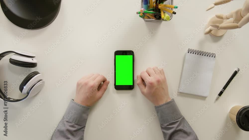A finger touching a green screen of the phone. The phone is on the white table. View from the top. Close-up. A finger touching a green screen of the phone. The phone is on the white table. View from the top. Close-up.