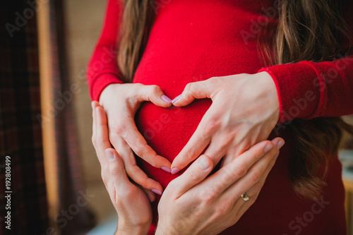 A pregnant girl hugs her tummy. A man is hugging the belly of a pregnant woman. Pregnant woman in a dress. Hands in the form of a heart on the stomach. Walking on the tummy of a pregnant woman