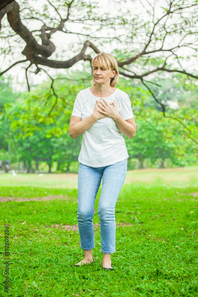 Heart attack concept. Senior woman suffering from chest pain outdoor in park,