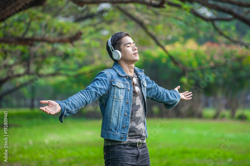 Asian young men Standextend the arms in nature, listen to music enjoy with headphones.