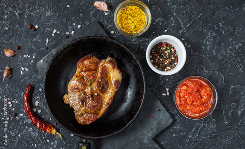 Juicy pork steak with spices on pan on dark stone background. Top