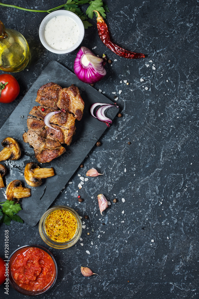Juicy pork steak with spices and grilled mushroomson dark stone background. Top view