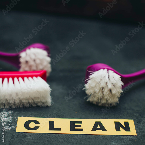 Cleaning house or office concept. Red and purple cleaning brushes, CLEAN inscription on a dark concrete background. Closeup