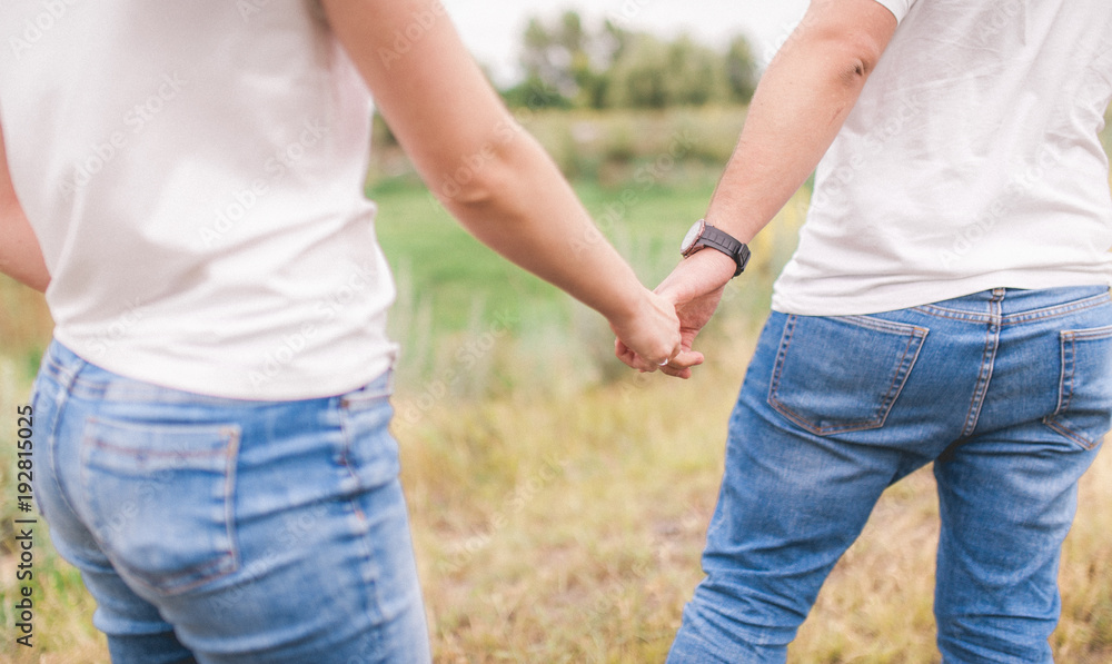 Girl and boyfriend hold hands. In blue jeans and white T-shirts, the pans on the arm have hours.