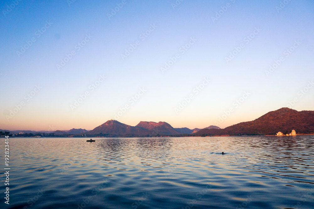 Serene dawn shot of fateh sagar lake udiapur india. The beautiful blue water with waves and the golden light striking the aravali hills in the distance make this one of the best places in Udaipur