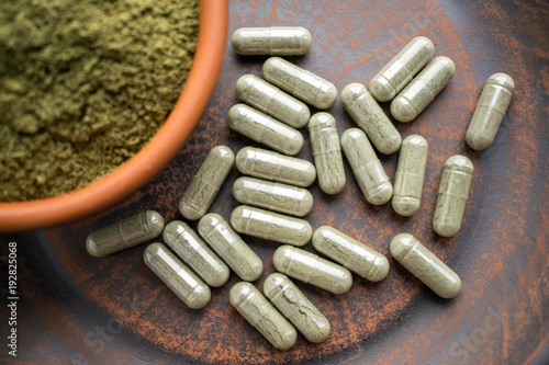 Close up Green capsules and powder on a clay brown plate on a burlap rustic background. Dietary supplements, vitamins and minerals for vegans and vegetarians. Healthy lifestyle, superfood photo