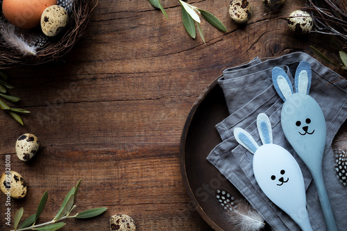 Easter frame for Web banners or greetings. Quail eggs, olive branches and a wooden plate with Easter bunny decorative spoons against rustic background photo