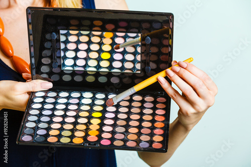Woman holds makeup eye shadows palette and brush.