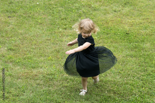 Girl with blond hair spin in black dress on grass