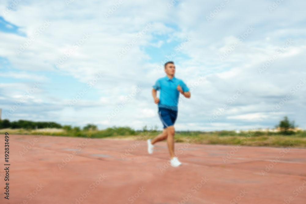 Young handsome active sportsman running on track field, blurred background