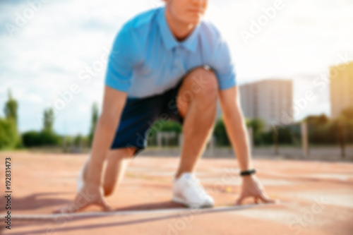 Sportsman about to start his run at the stadium, zoomed ithout face, blurred background.