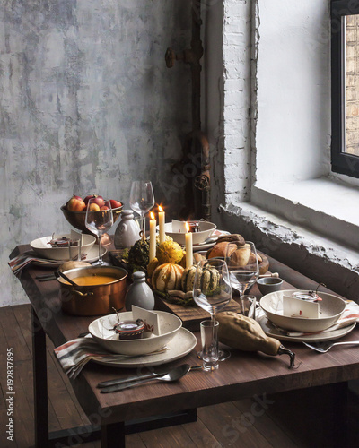 Rustic table setting with pumpkin soup and pumpkins on the background of the window in the loft