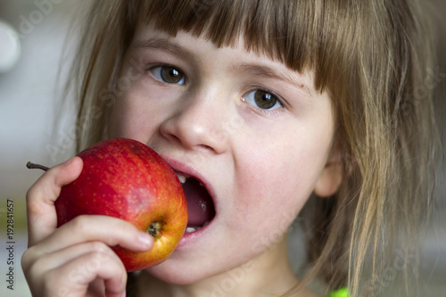 Cuadro en lienzo A cute little curly toothless girl smiles and holds a red apple