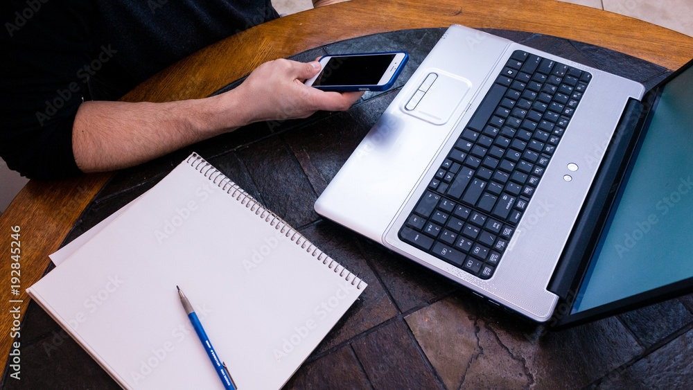 Male hands typing on phone while sitting at laptop pc and typing on his phone Male hands typing on phone while sitting at laptop pc and typing on his phone