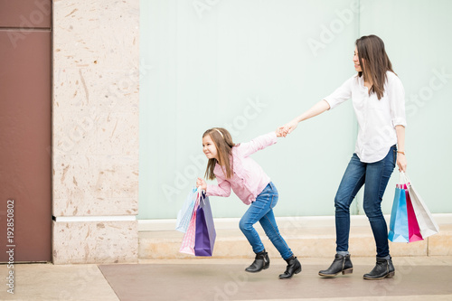 Bilde på lerret Little girl pulling her shopaholic mother out off a store