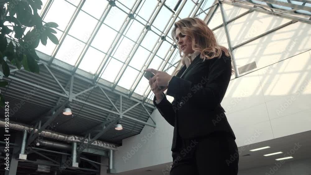 young woman in a business suit uses a mobile phone. business woman is texting a message on the smartphone in the office building. young woman in a business suit uses a mobile phone. business woman is texting a message on the smartphone in the office building.