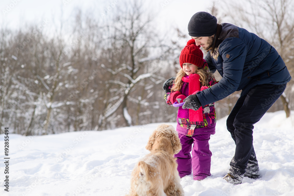 Obraz premium Father and daughter train their dog during winter walk