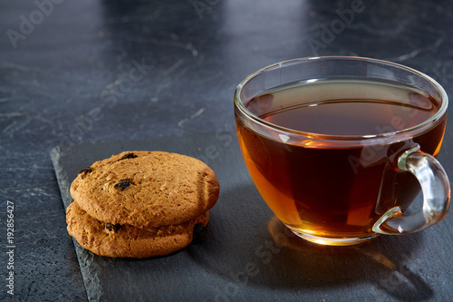 Shallow depth of field photo of a glass cup of black tea with brownies on a dark greyish marble background.