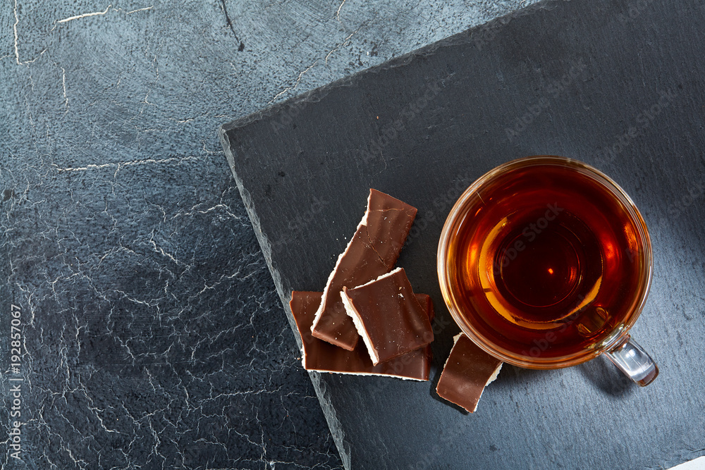 glass cup of black tea with chocolate pieces on a dark greyish marble background. Top view
