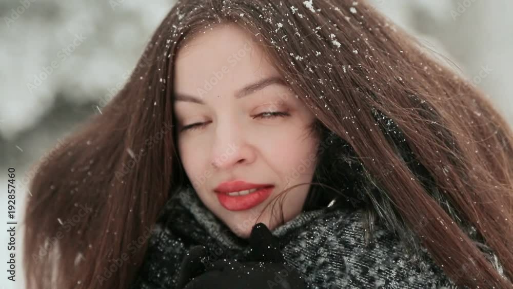 A beautiful young girl with chic long hair is enjoying falling snow in winter. Face close-up. A beautiful young girl with chic long hair is enjoying falling snow in winter. Face close-up.