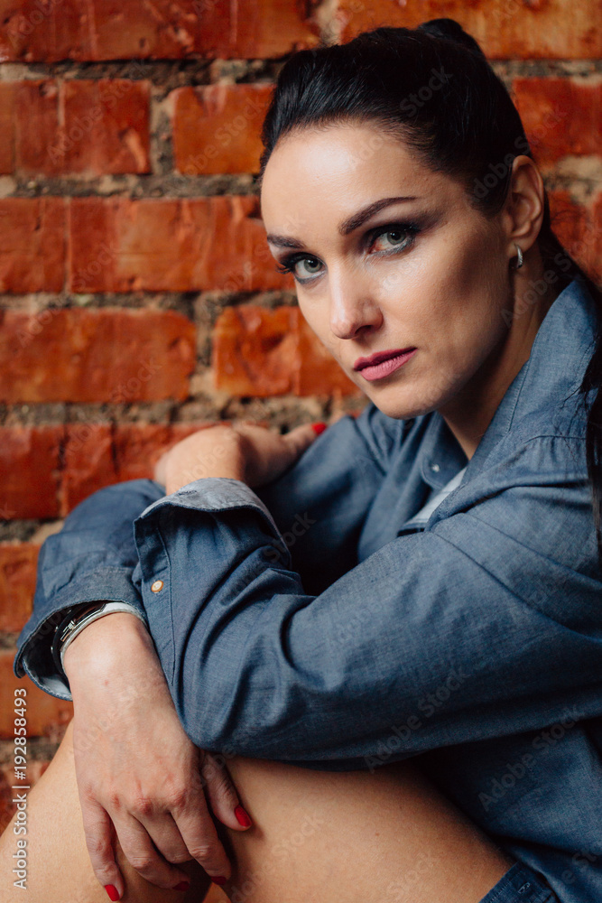 Fototapeta premium Pretty brunette woman in shirt sitting on the floor near brick wall. Gorgeous sexy girl