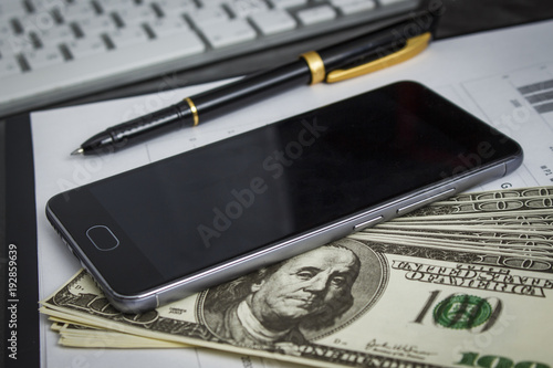 Black ballpoint pen with a bunch of dollars and a mobile phone