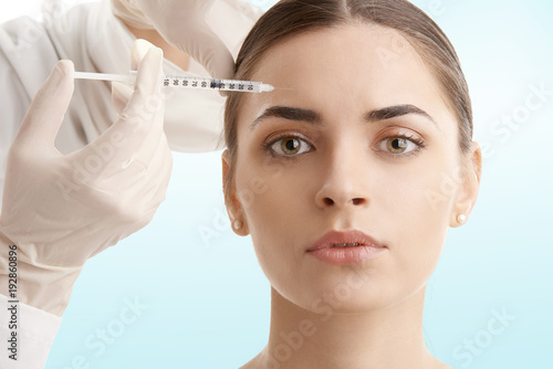 Woman at plastic surgery. Portrait of an attractive young woman receiving botox treatment. Isolated on light blue background.
