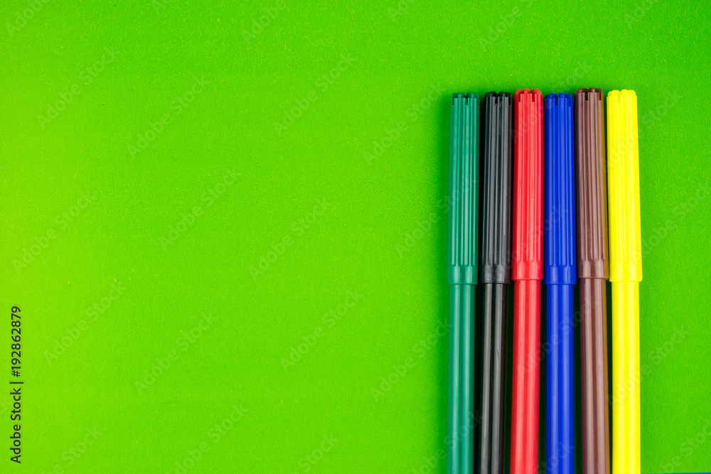 Fototapeta premium A set of different colors of felt-tip pens on a green background.