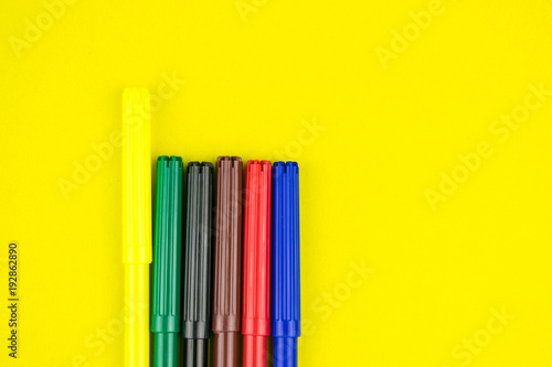 A set of different colored felt-tip pens on a yellow background.