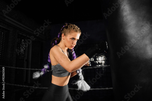 Young woman trains in boxing ring with heavy punching bag. © photominus21