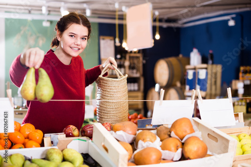 Portrait of brunette girl buying ripe pear in supermarket