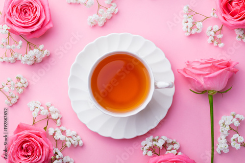 Cup of tea with fresh flowers on pink background. Top view. Copy space