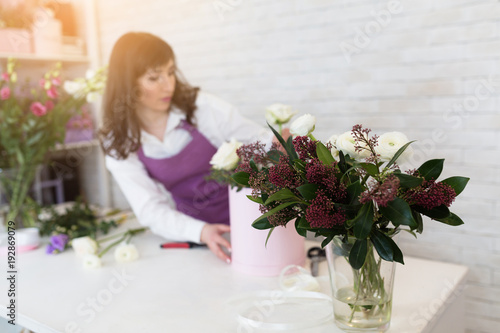 Beautiful young florist makes a nice bouquet in a box in own flower shop