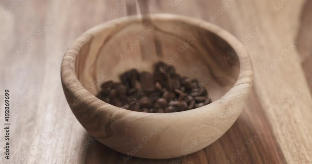 Slow motion coffee beans falling into wood bowl on table