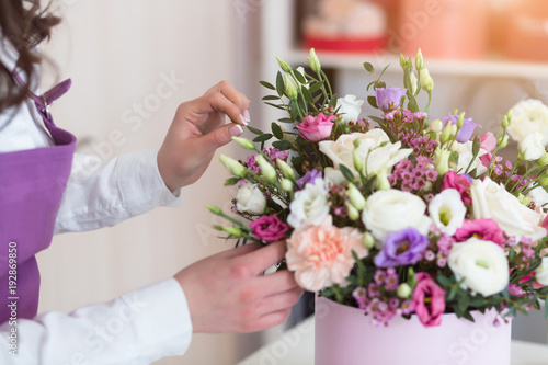 Florist workplace. Young woman arranging a beautiful bouquet with white roses, eustomas, leaves, ranunculus flowers and gypsophila in flower shop.