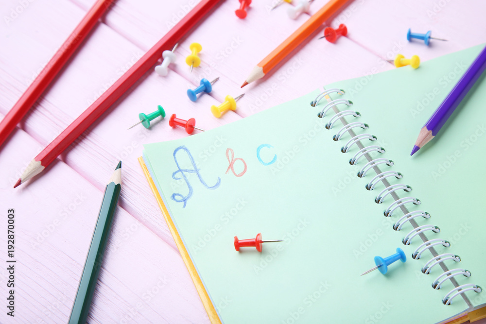 Handwritten letters ABC in notebook with stationery on pink wooden table Handwritten letters ABC in notebook with stationery on pink wooden table