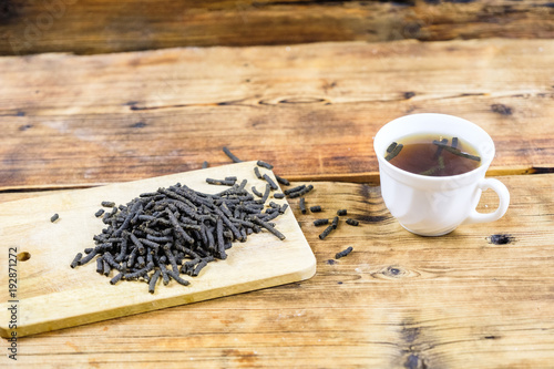 Close-up fermented Ivan-tea on wooden board. Dry herbal natural tea. White cup with Ivan-tea.