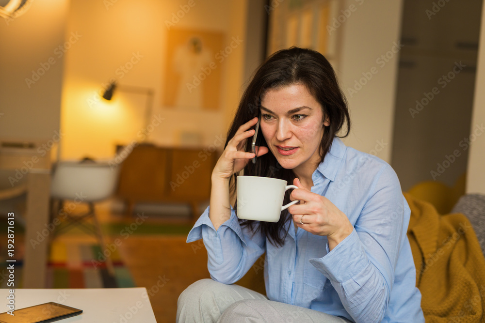 Always on line with her friends with her friends. Woman talking on mobile phone and drinking coffee in her living room Always on line with her friends with her friends. Woman talking on mobile phone and drinking coffee in her living room
