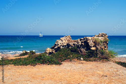 Ruins of a wall on the beach with a sailboat